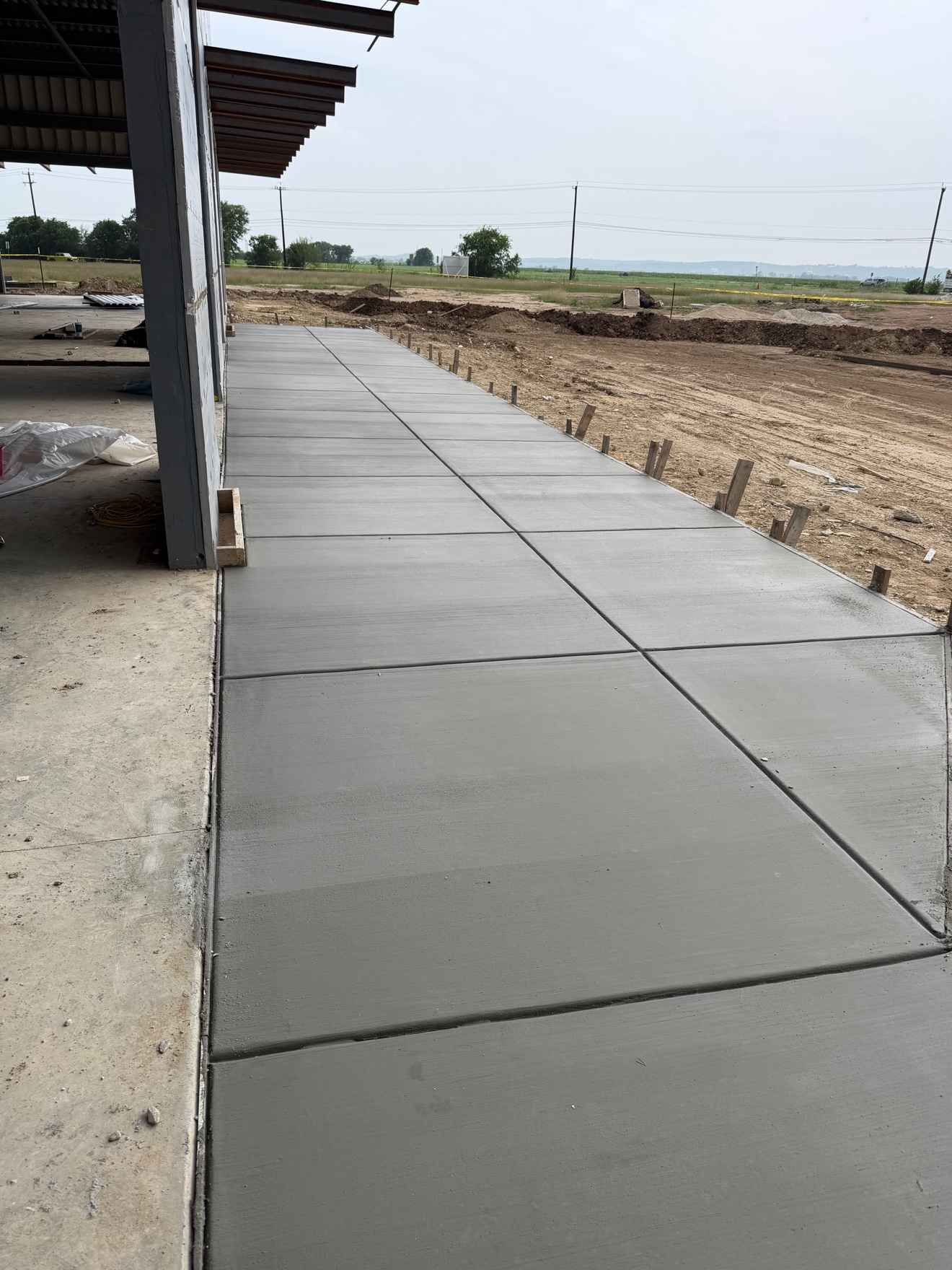 Long, freshly poured commercial concrete sidewalk beside a building under construction
