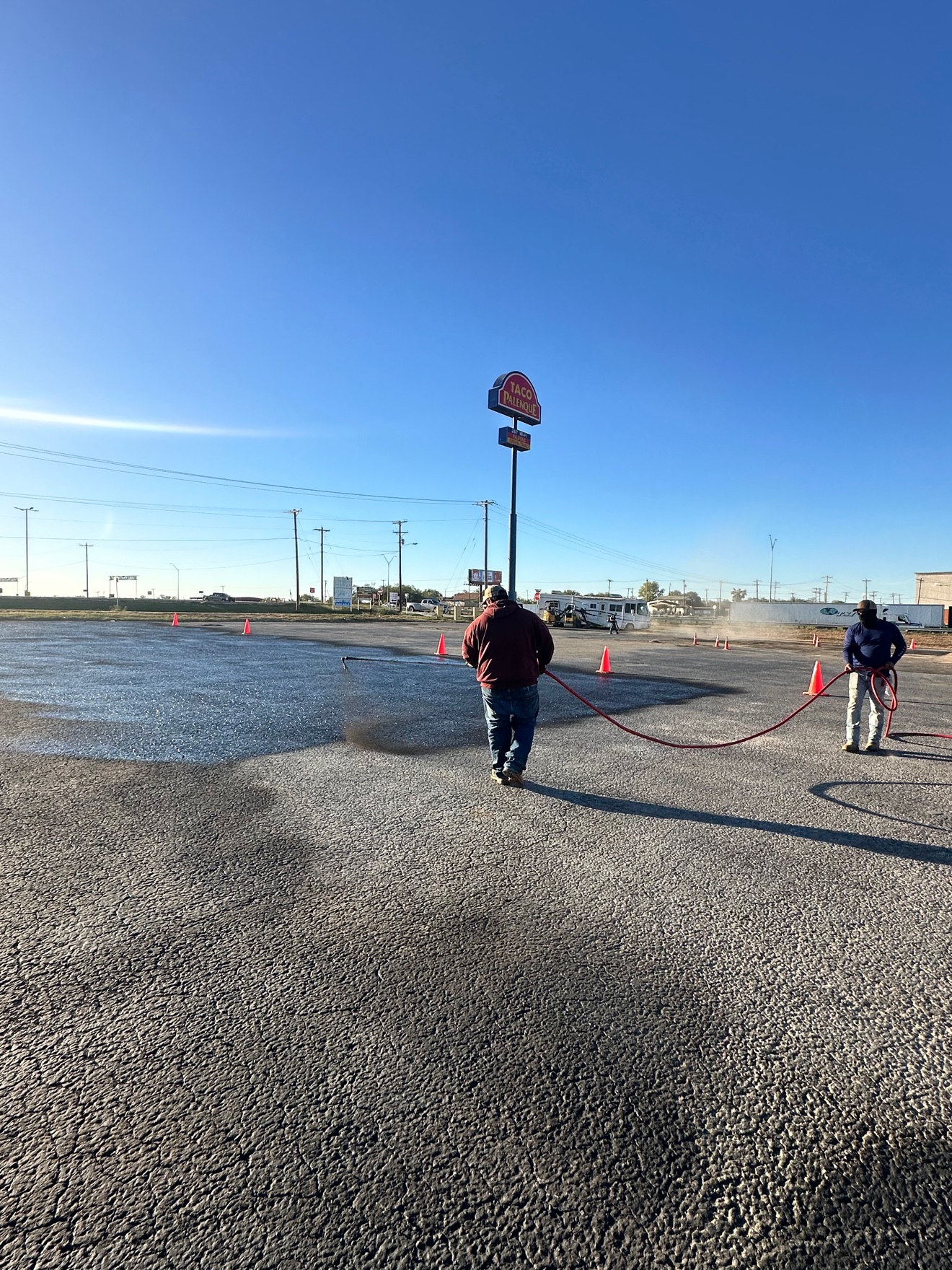 Crew member spraying sealcoat on an asphalt parking lot
