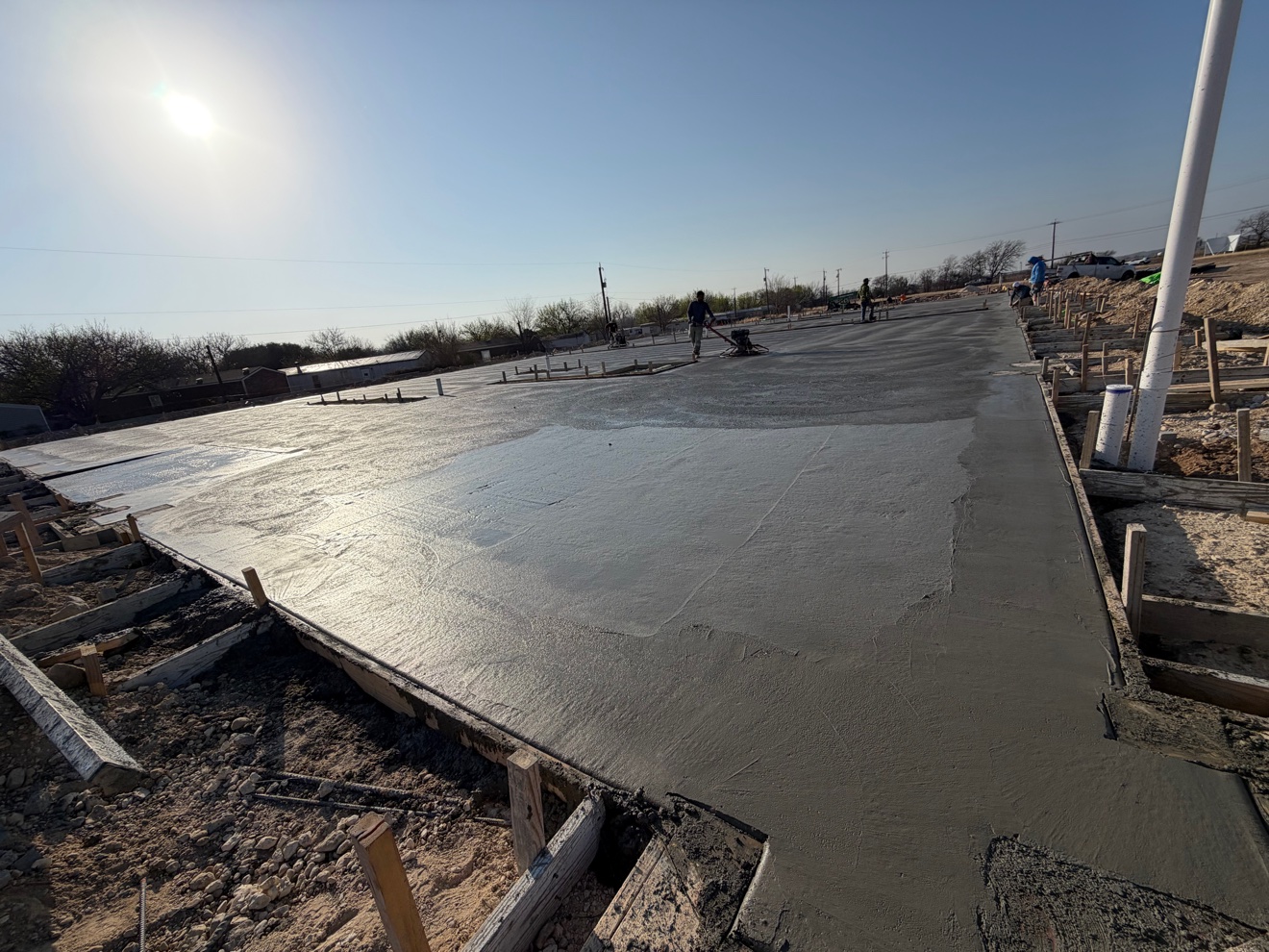 Crew power-troweling a large concrete slab under a bright sun