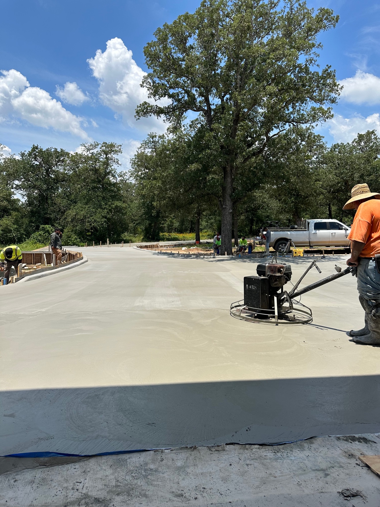 Crew member power-troweling a fresh concrete driveway at a stone house