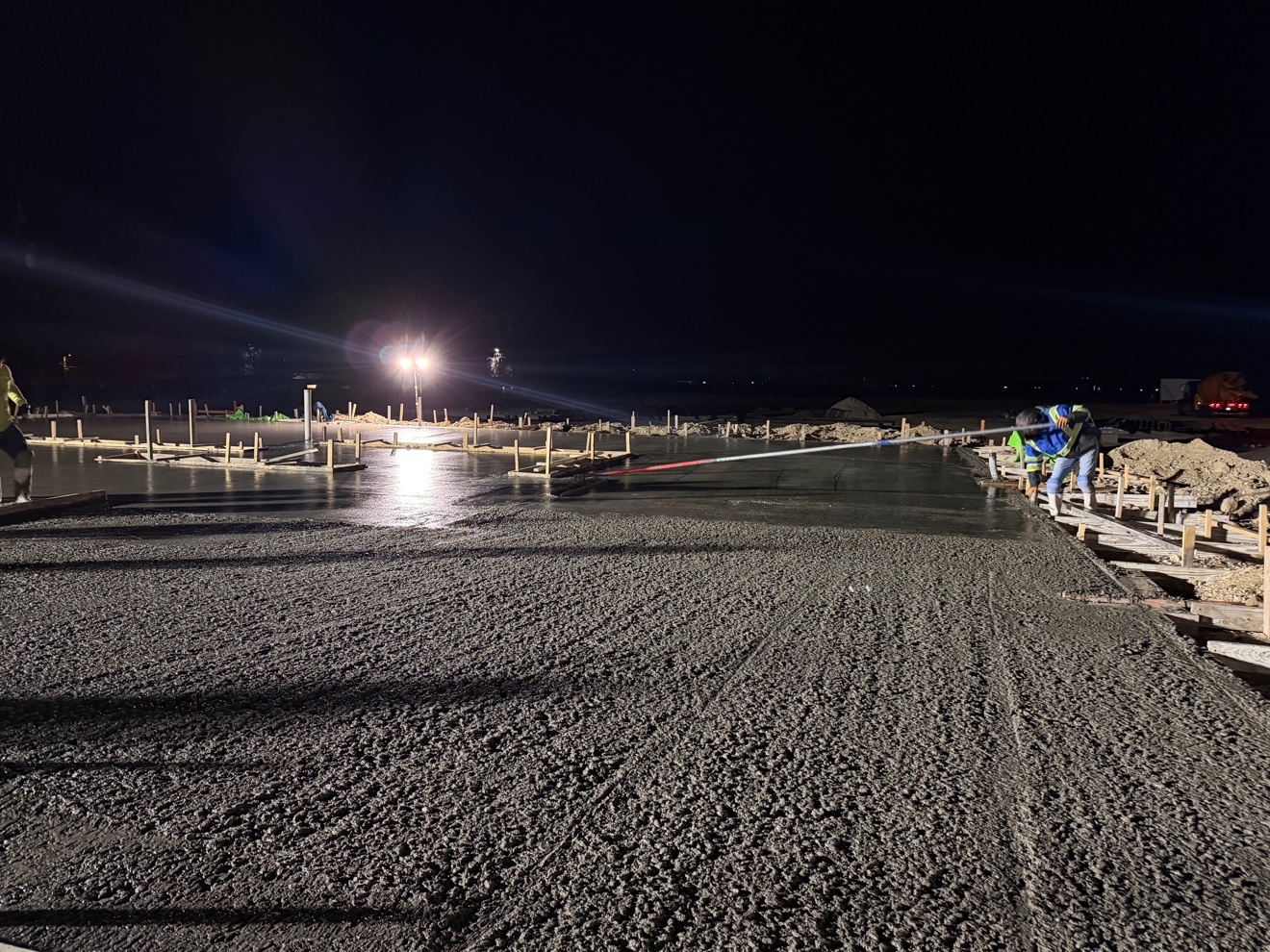 Crew screeding fresh concrete on a night pour under work lights