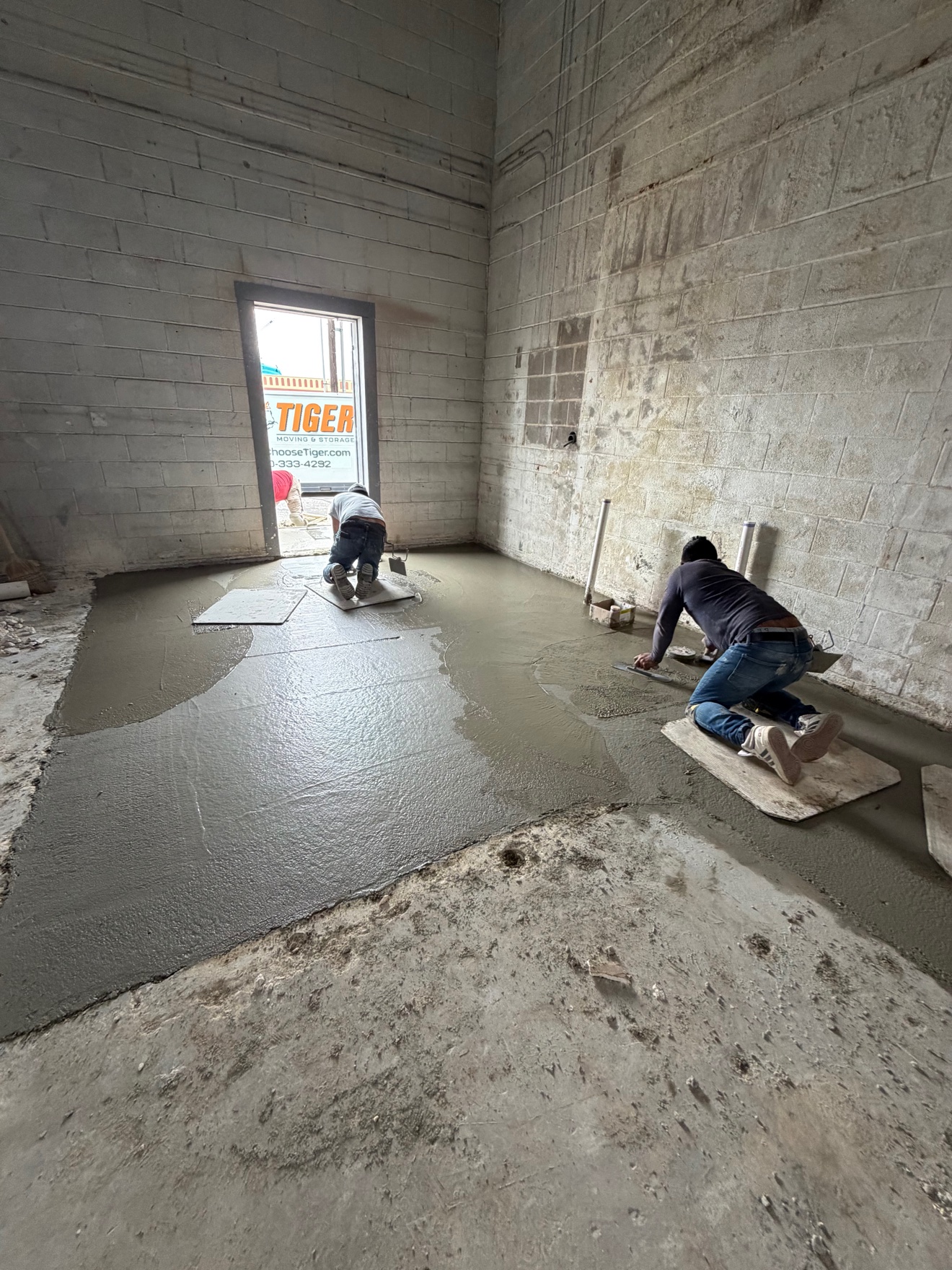 Crew hand-finishing a fresh interior concrete floor inside a block building