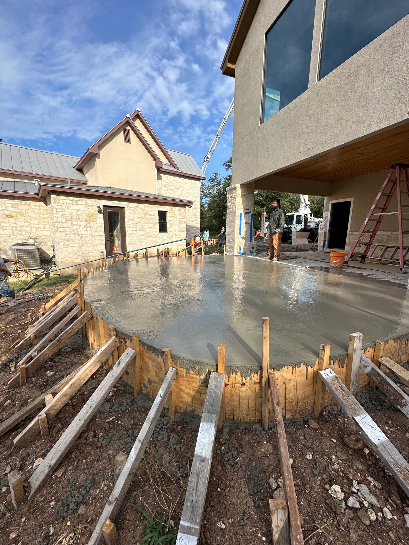 Freshly poured curved concrete patio beside a stone house