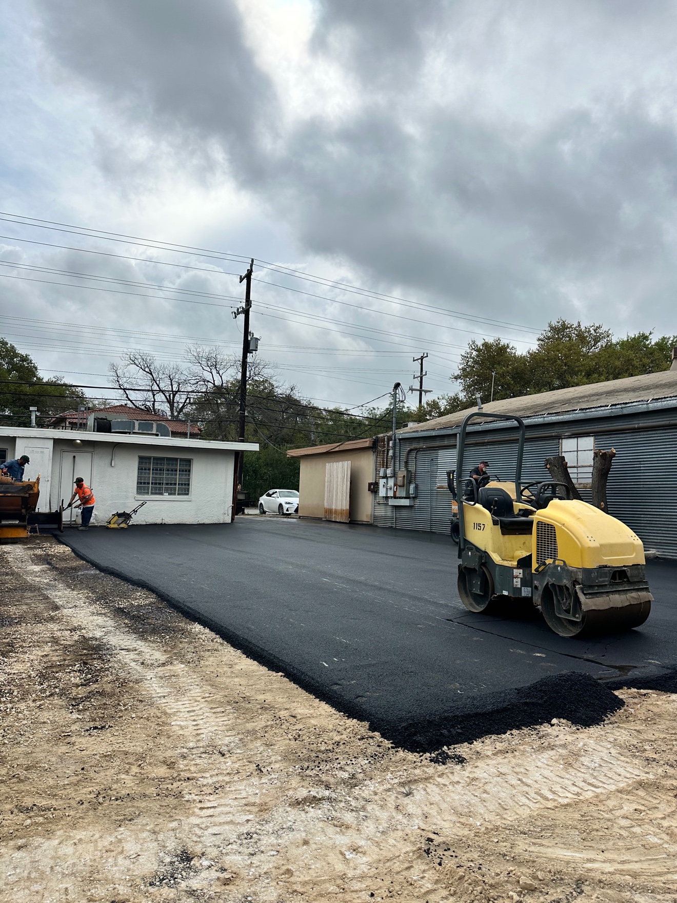 Yellow roller compacting freshly laid asphalt while the crew works nearby
