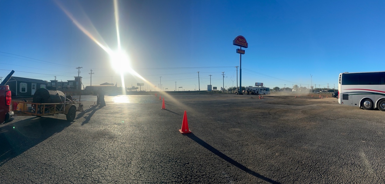 Freshly sealcoated asphalt parking lot under a clear sky