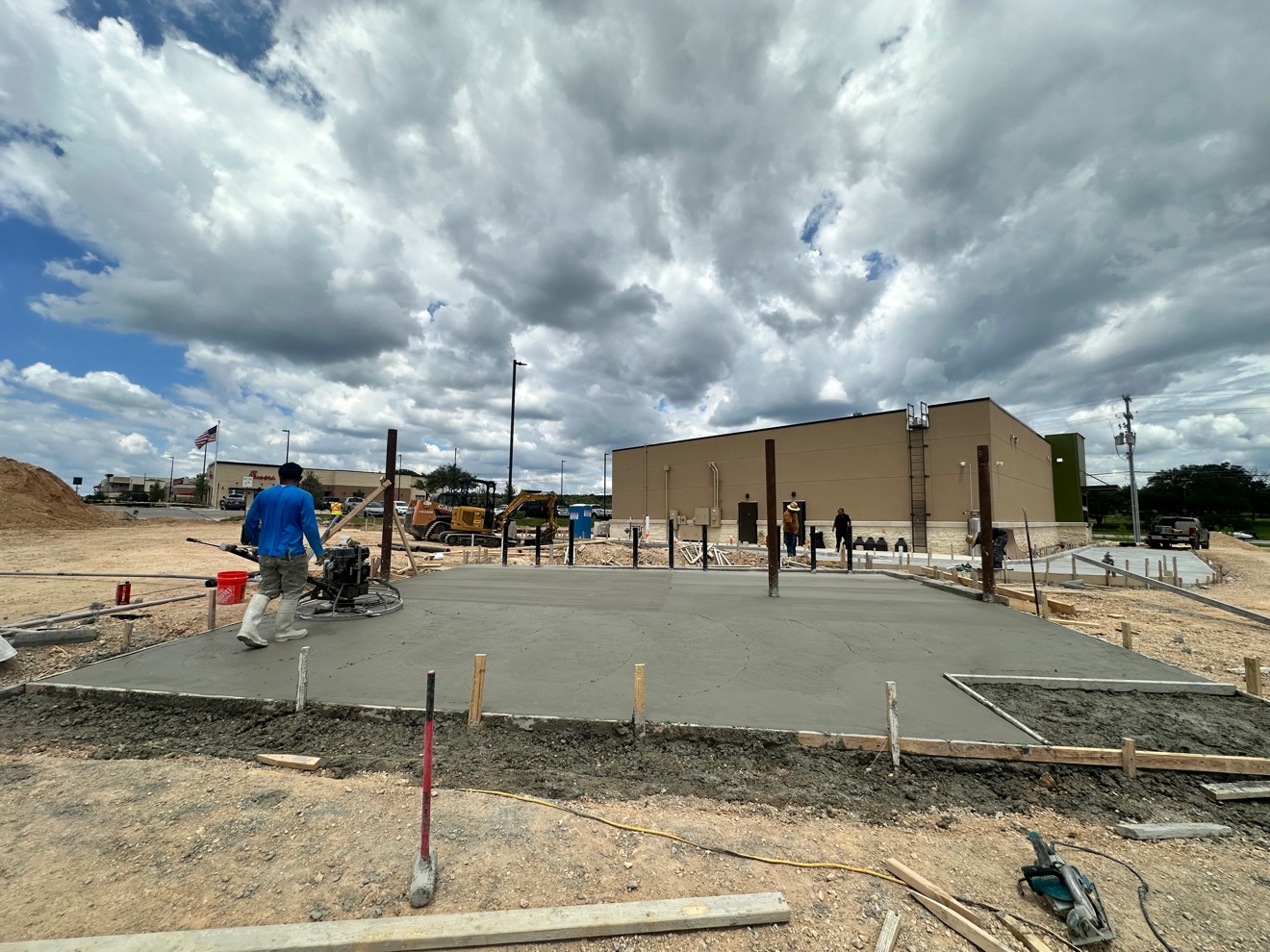 Crew member power-troweling a fresh concrete pad at a commercial job site
